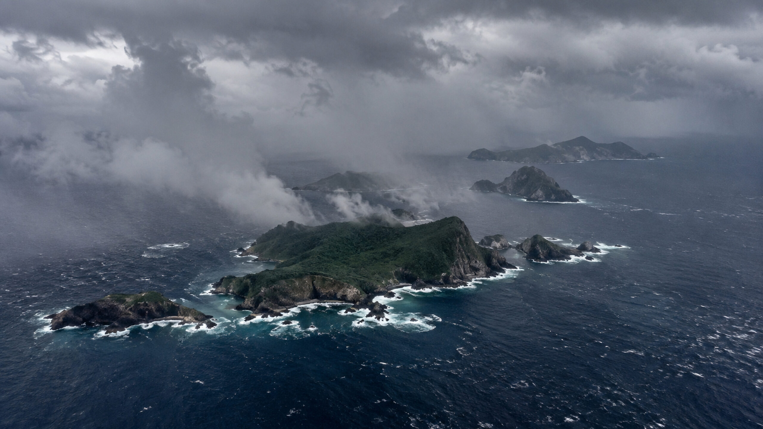 Photorealistic editorial illustration of a remote western Pacific island chain beneath heavy tropical rain and rough seas