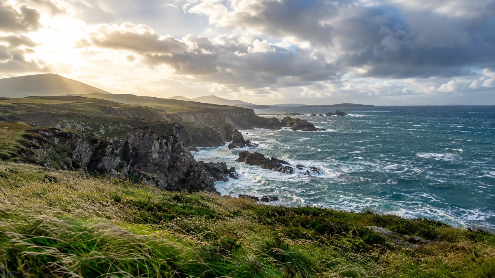 Rugged Atlantic-style European coastline under layered clouds and changing sunlight.
