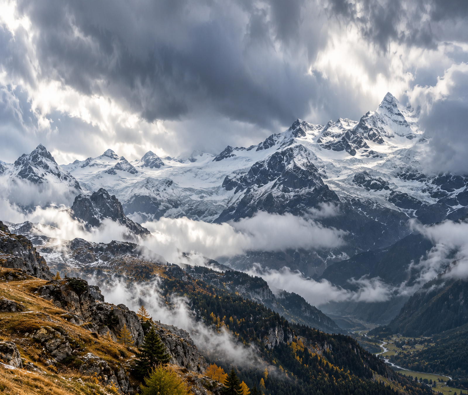 Symbolic wide Alpine landscape with fresh snow on high ridges, autumn valleys, low cloud and mixed rain and snow during a cold front.